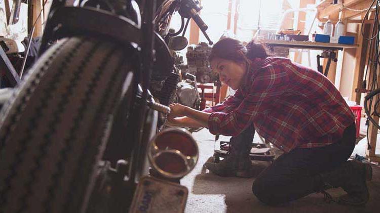 一个女人在车库里跪着修摩托车.