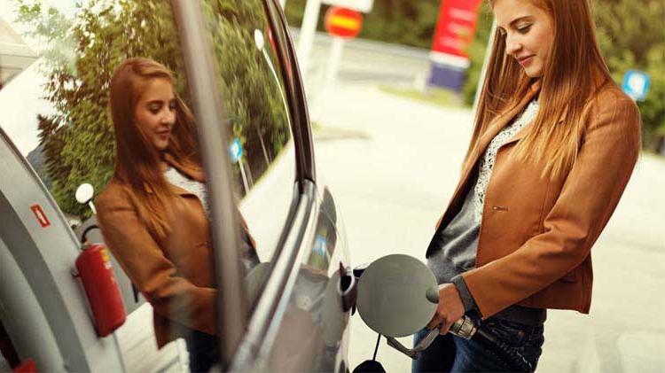 Young woman st和ing outside putting gas in her car.